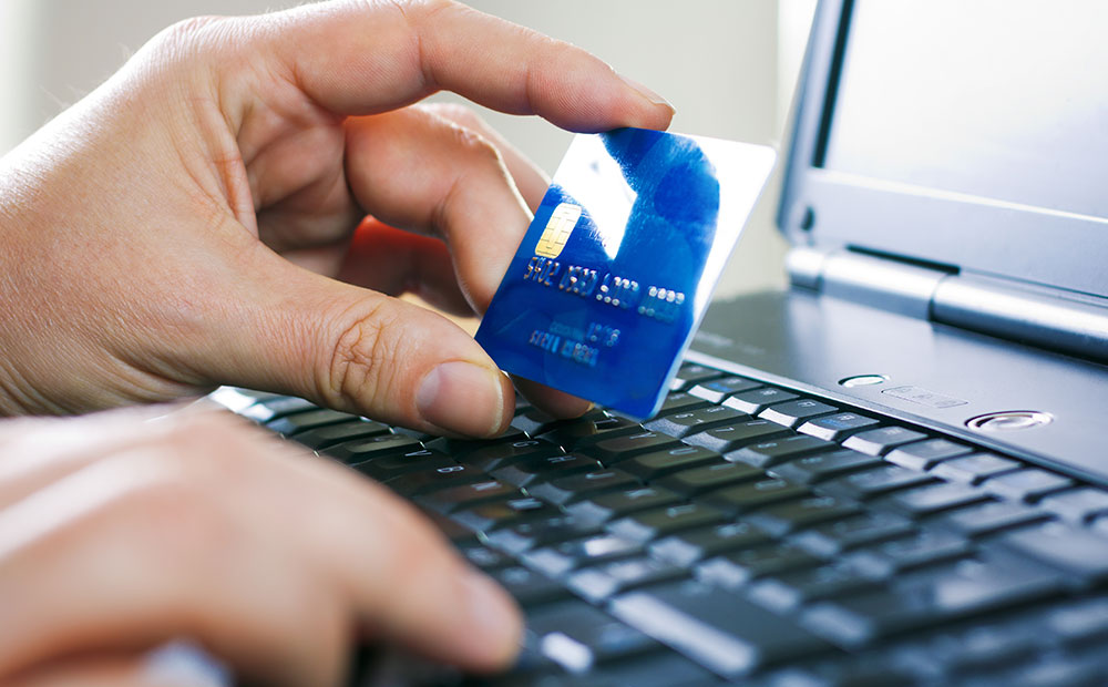 birinde kredi kartı bulunan iki insan eli ile bir laptop bulunan görsel 